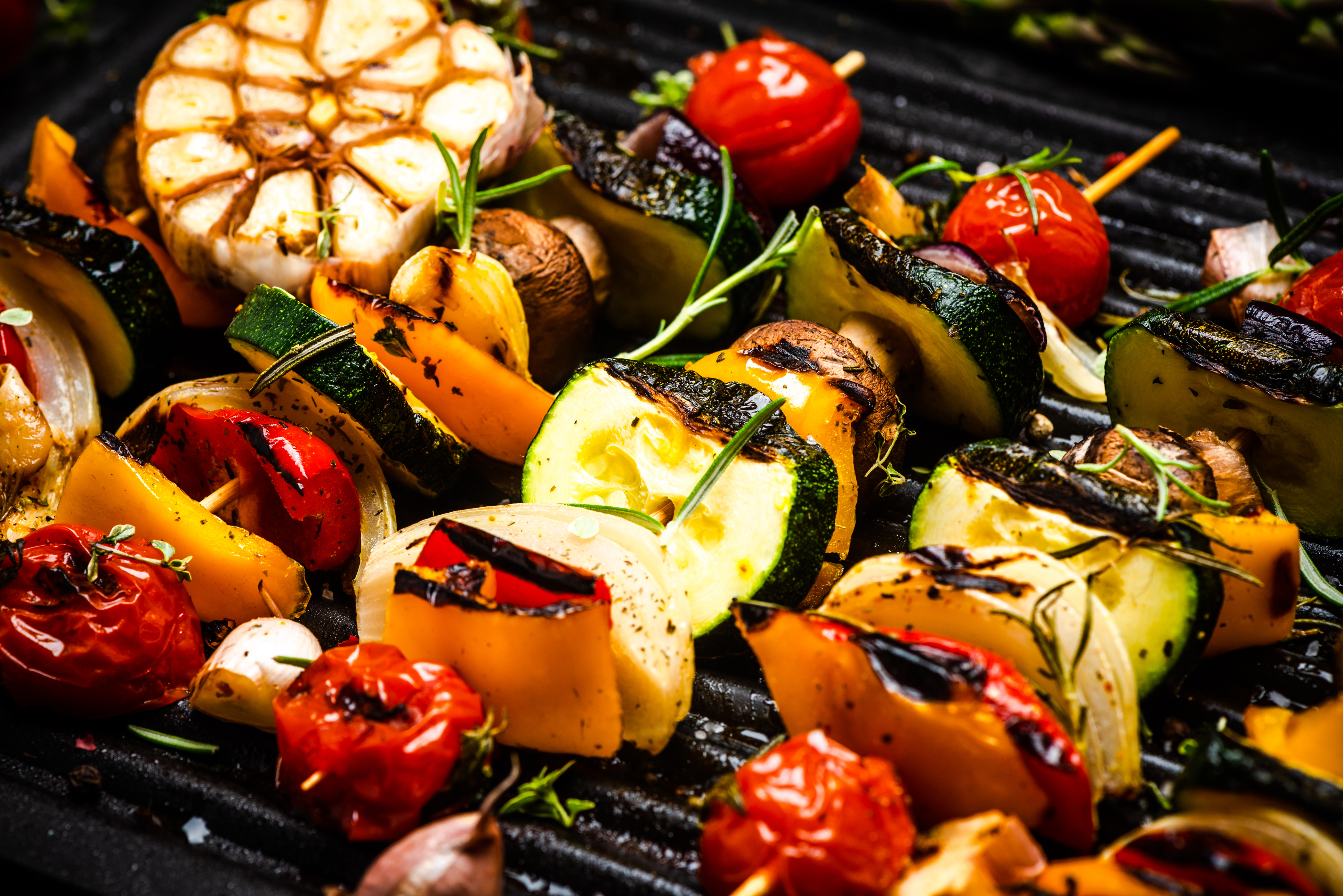 An image of grilled vegetables on skewers, seasoned with herbs, on a BBQ.